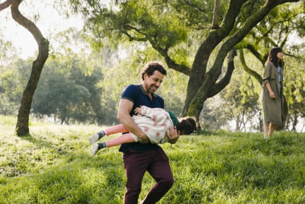 A father holding and swinging a child around in a green outdoor setting.