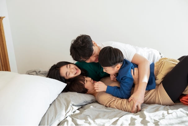 A family of four playing together on the bed.