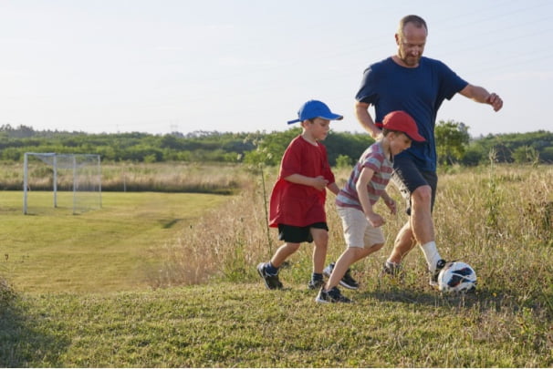 A father and two boys kick around a soccer ball.